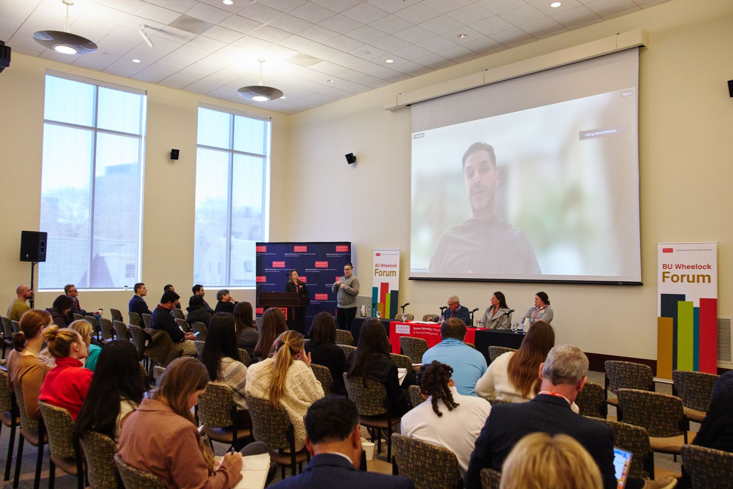 Kamal Bahamdan speaking over zoom on a projector during the panel: Sport Psychology Insights from an Athlete, Coach, and Consultant