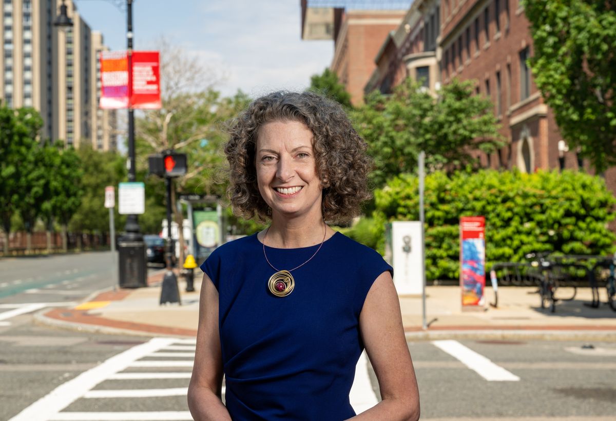 Dean Penny Bishop stands smiling in front of Silber Way in Boston Massachusetts with BU Wheelock in the background