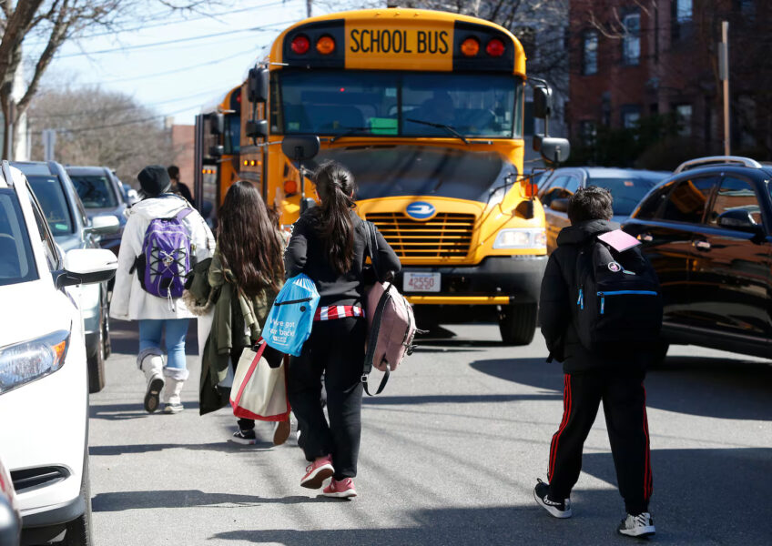 Children walking down the street next to a school bus.