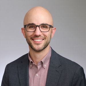 Shows Rob Martinelle, who is wearing glasses, a reddish collared shirt, and a gray jacket