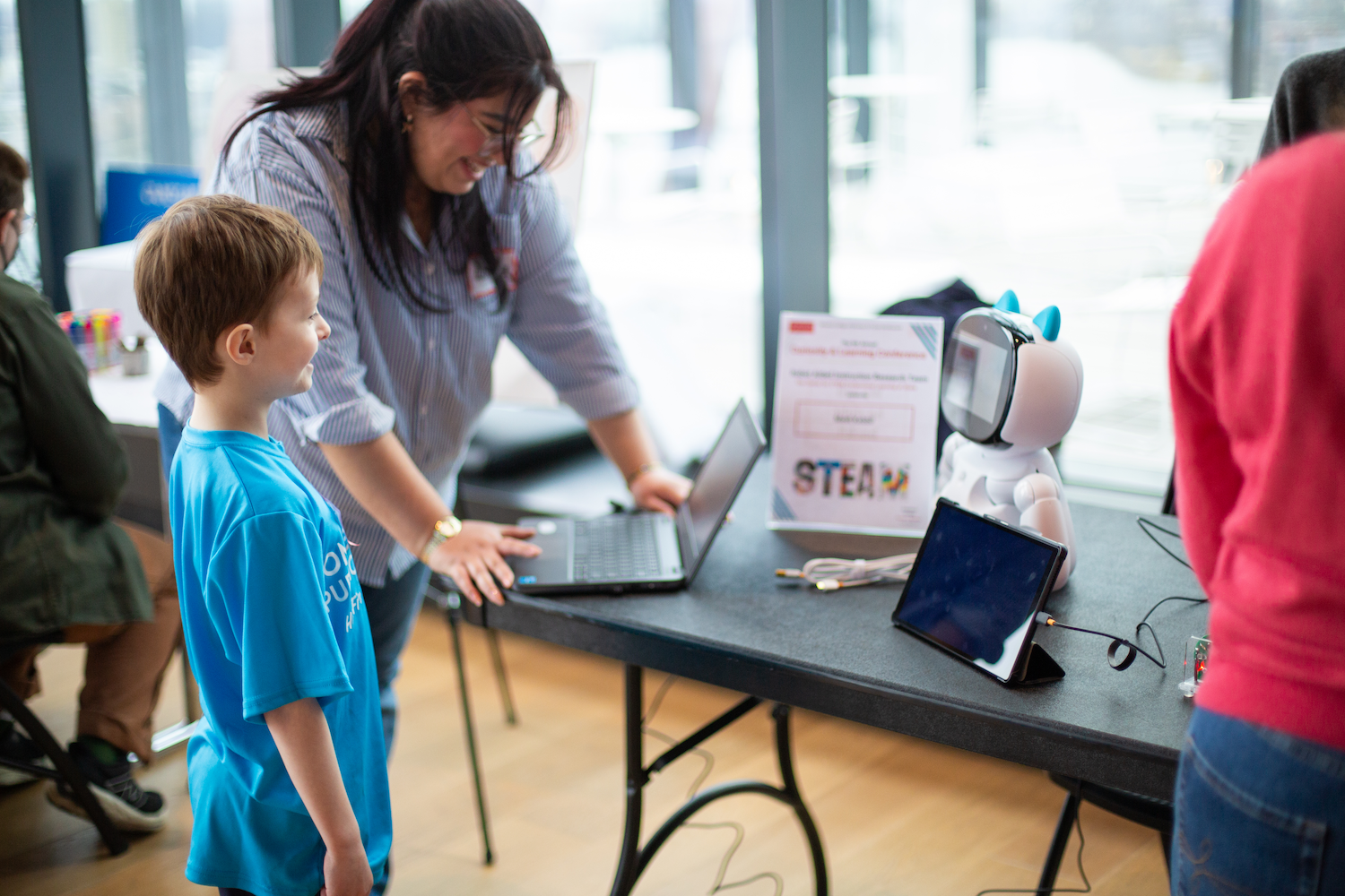 Women and boy smiling as they interact with a educational robot at the 2024 Curiosity & Learning Conference