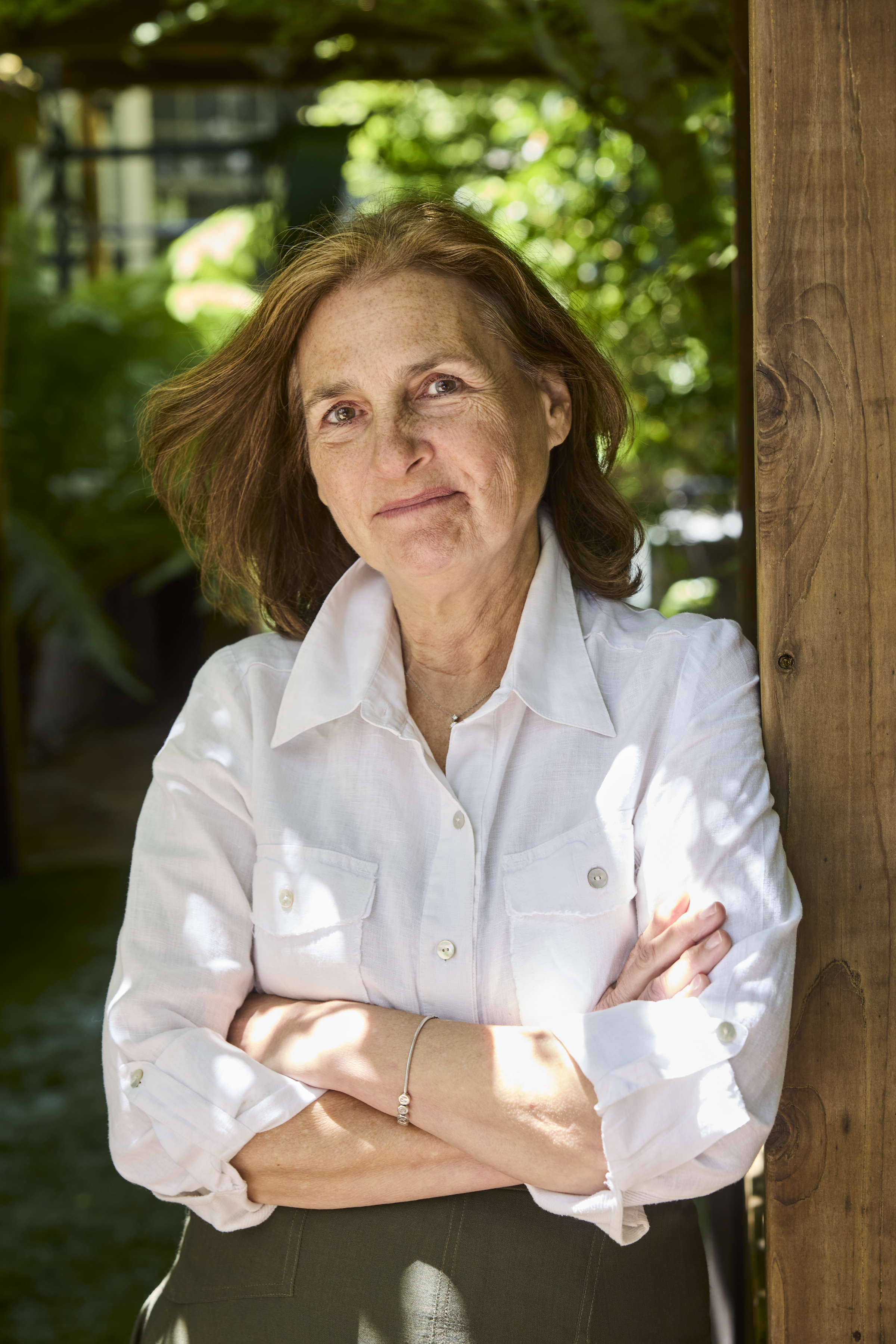 Deb Buehler stands smiling in a white button down leaning on a wooden beam