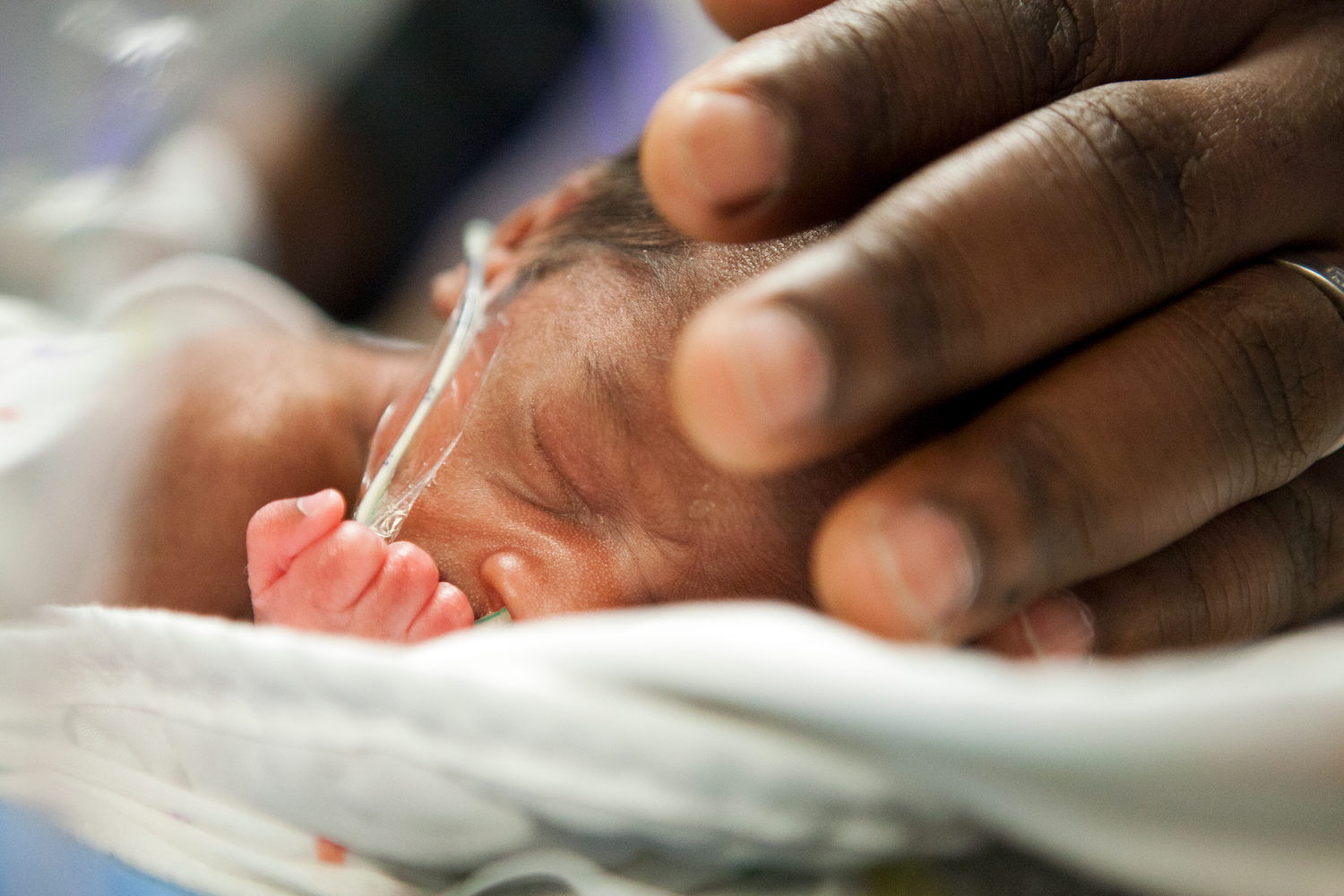 Photo of hand touching premature baby in NICU