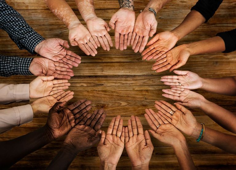 A circle of palms up hands of a diverse group.