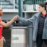 Photo: Two woman fist bumping each other at a track meet. Reigning Patriot League Indoor Women’s Field Athlete of the Meet Peace Omonzane (CAS’26) fistbumps jumps and multis coach Sara Macey.